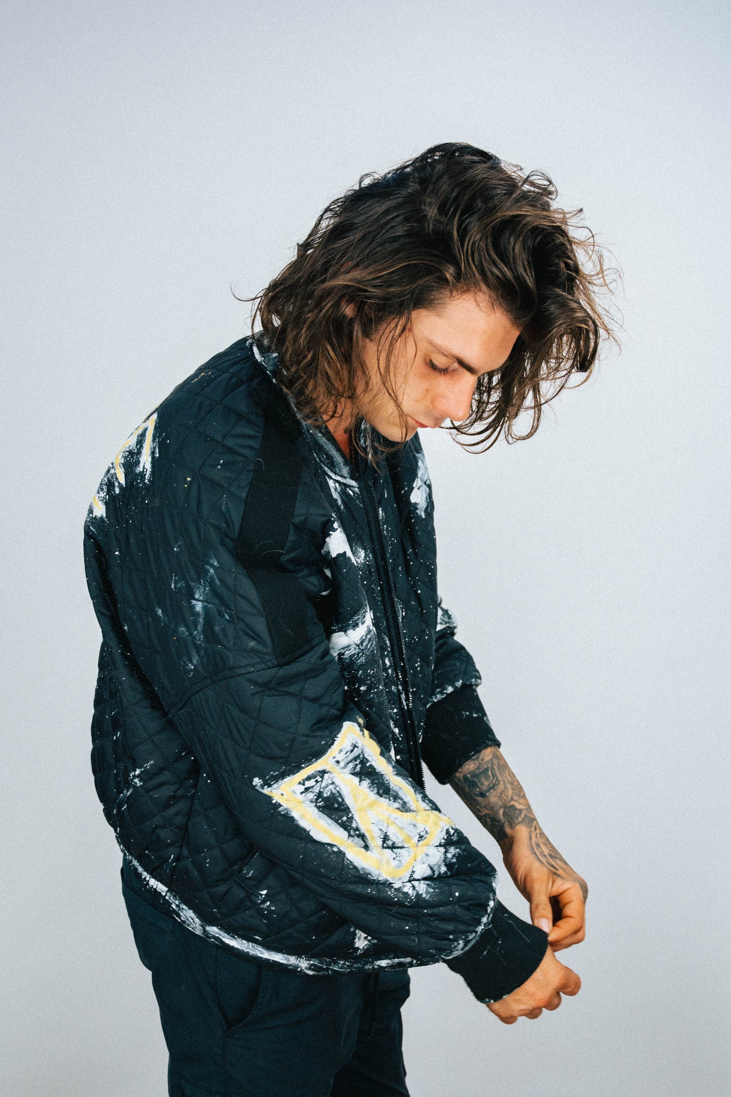 Person wearing a black quilted bomber jacket with white and yellow spray painted and hand painted designs on a plain background