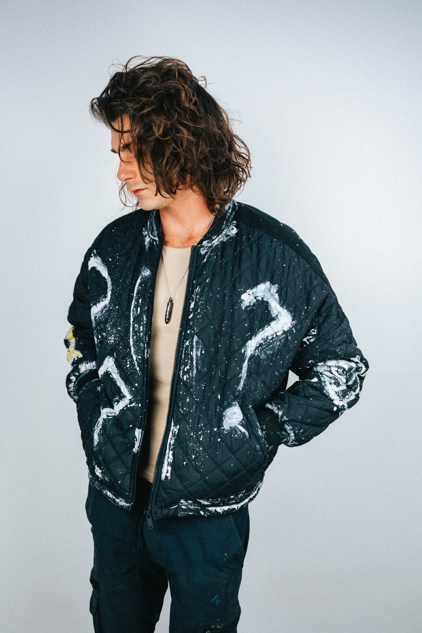 Person wearing a black quilted bomber jacket with white and yellow spray painted designs on a plain background
