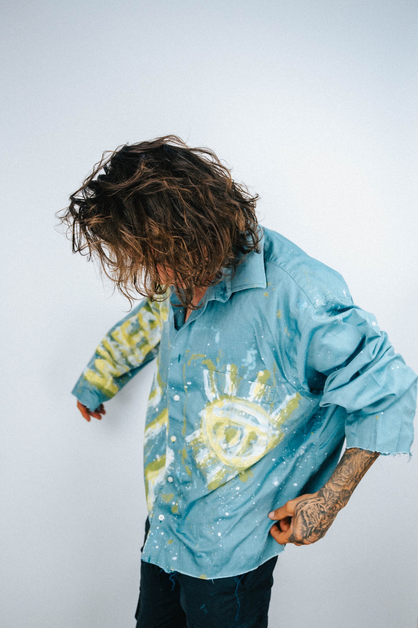 Man wearing a light blue shirt with abstract white and yellow spray painted designs on a plain background