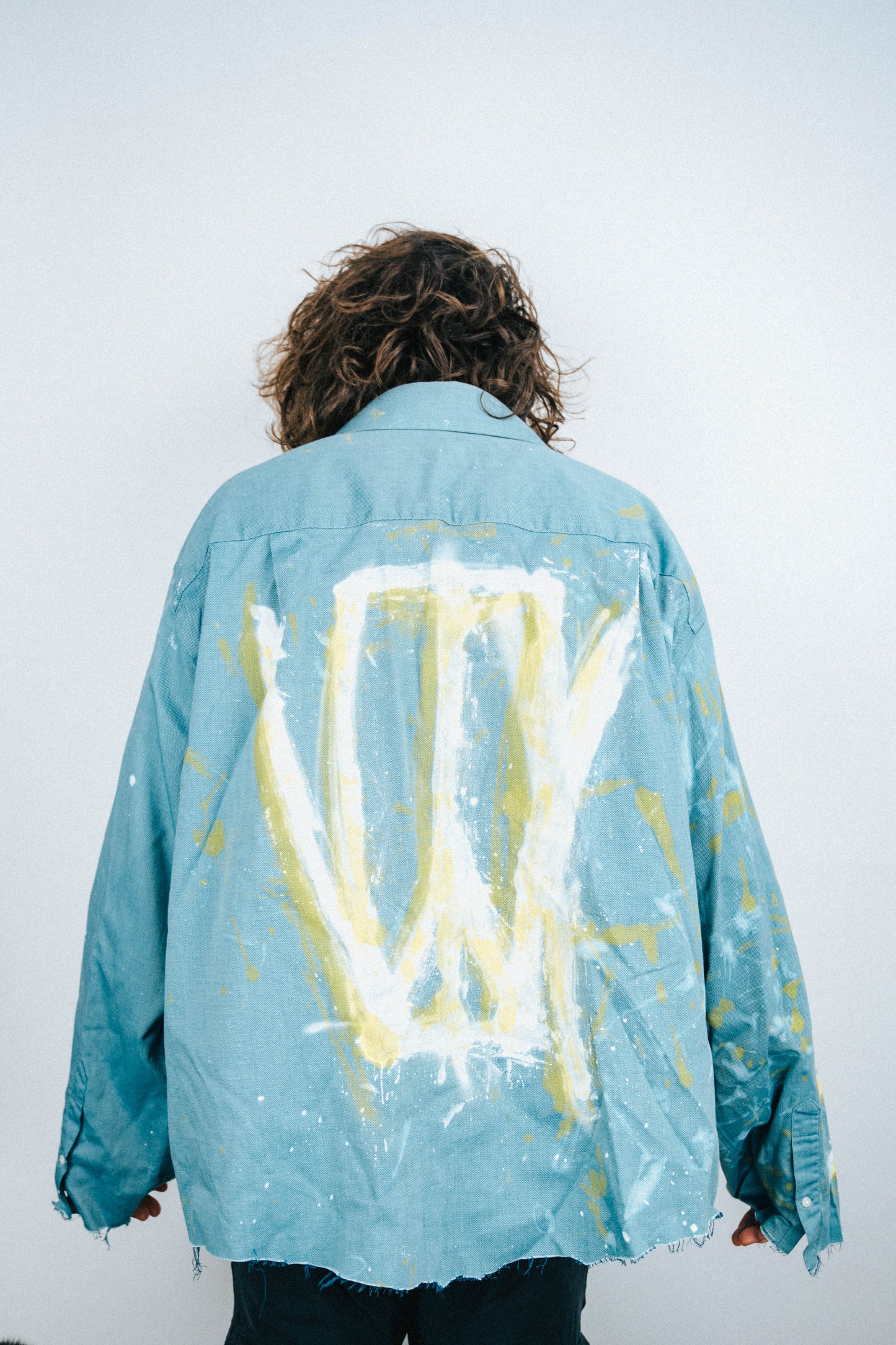 Man wearing a light blue shirt with abstract white and yellow spray painted designs on a plain background