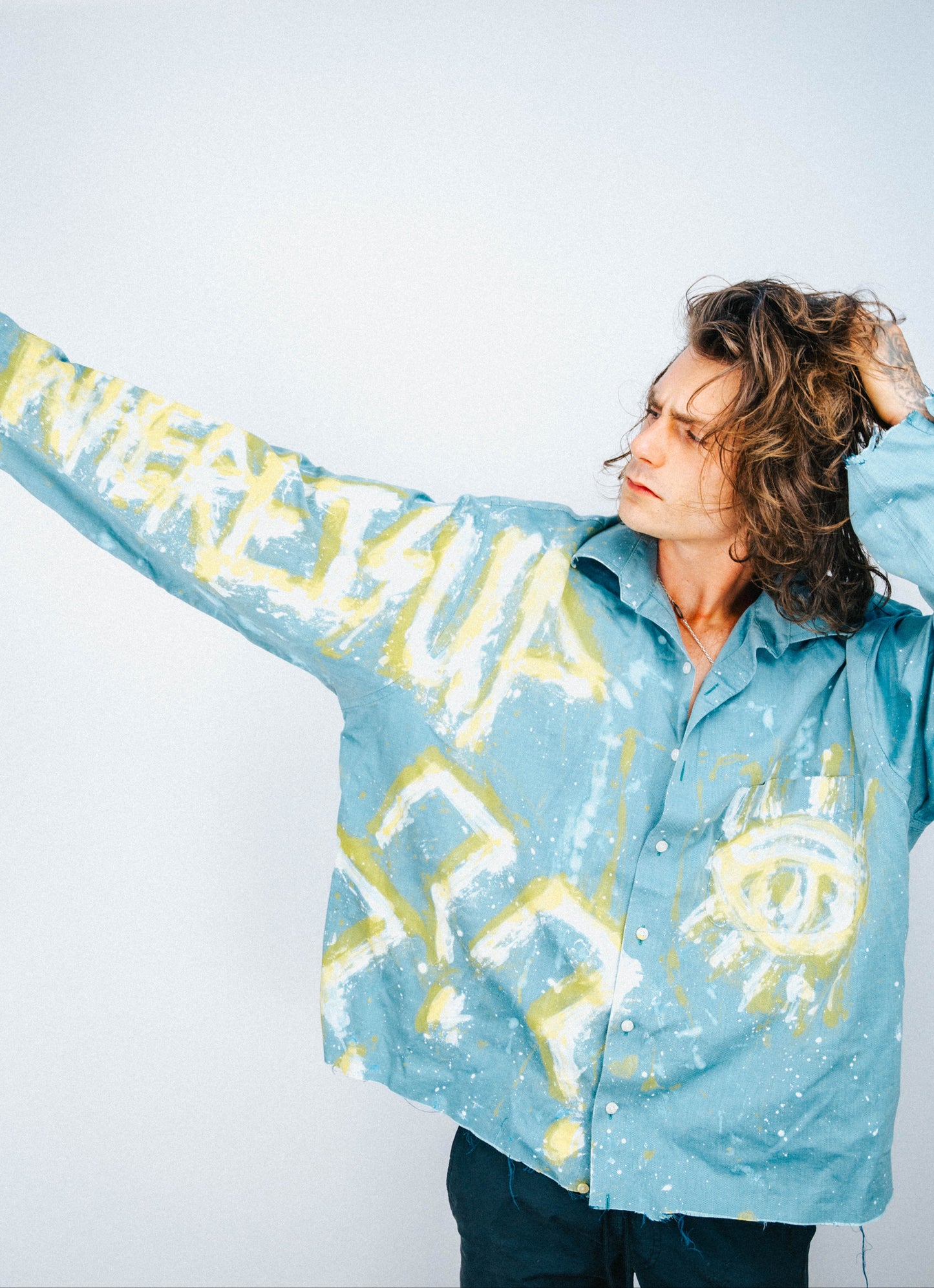 Man wearing a light blue shirt with abstract white and yellow spray painted designs on a plain background