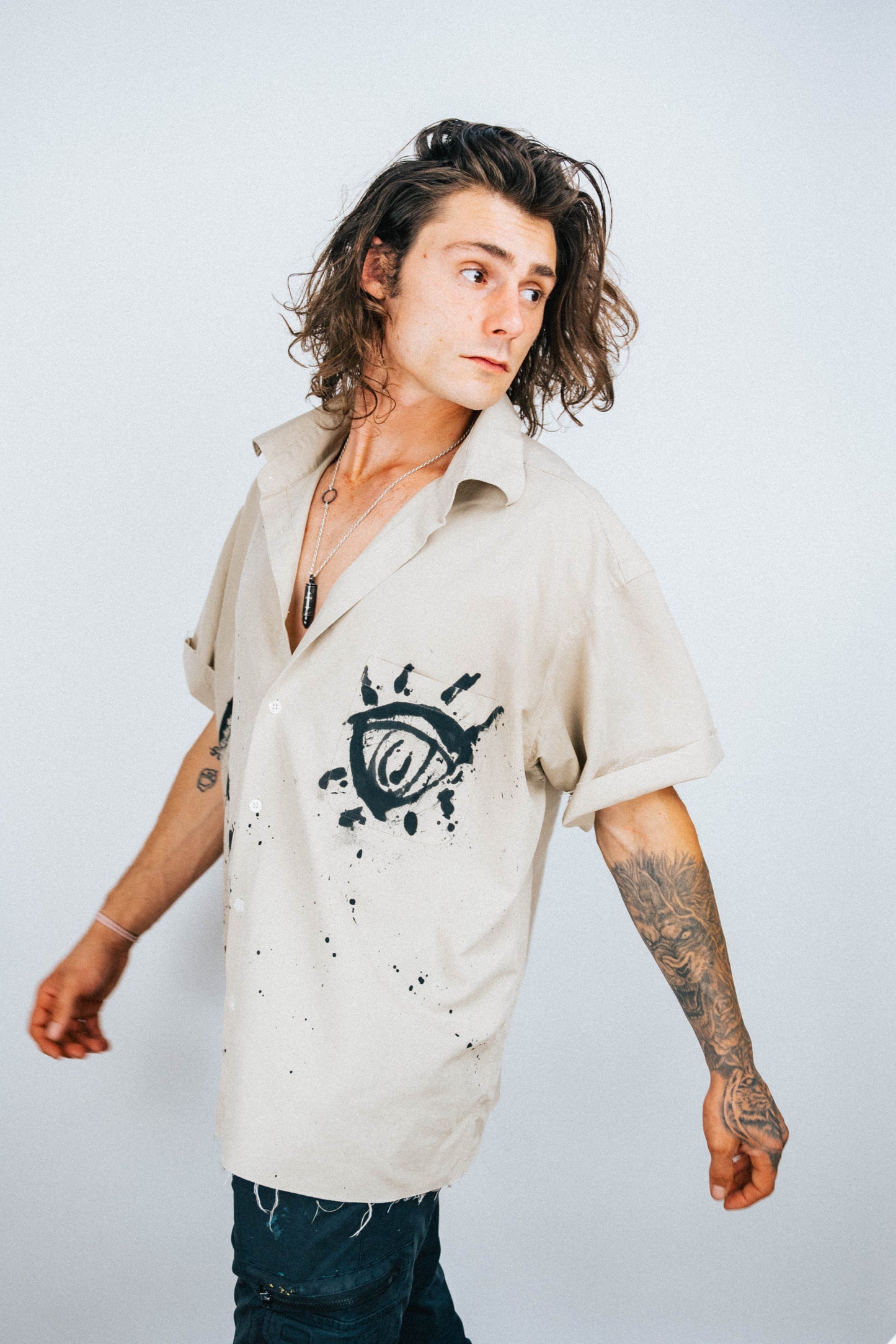 Person wearing a tan button-up shirt with black eye spray painted designs on a plain background