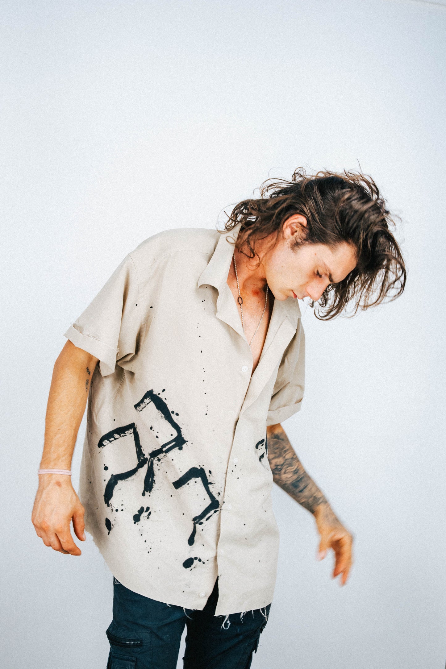 Person wearing a tan button-up shirt with black spray painted question mark designs on a plain background