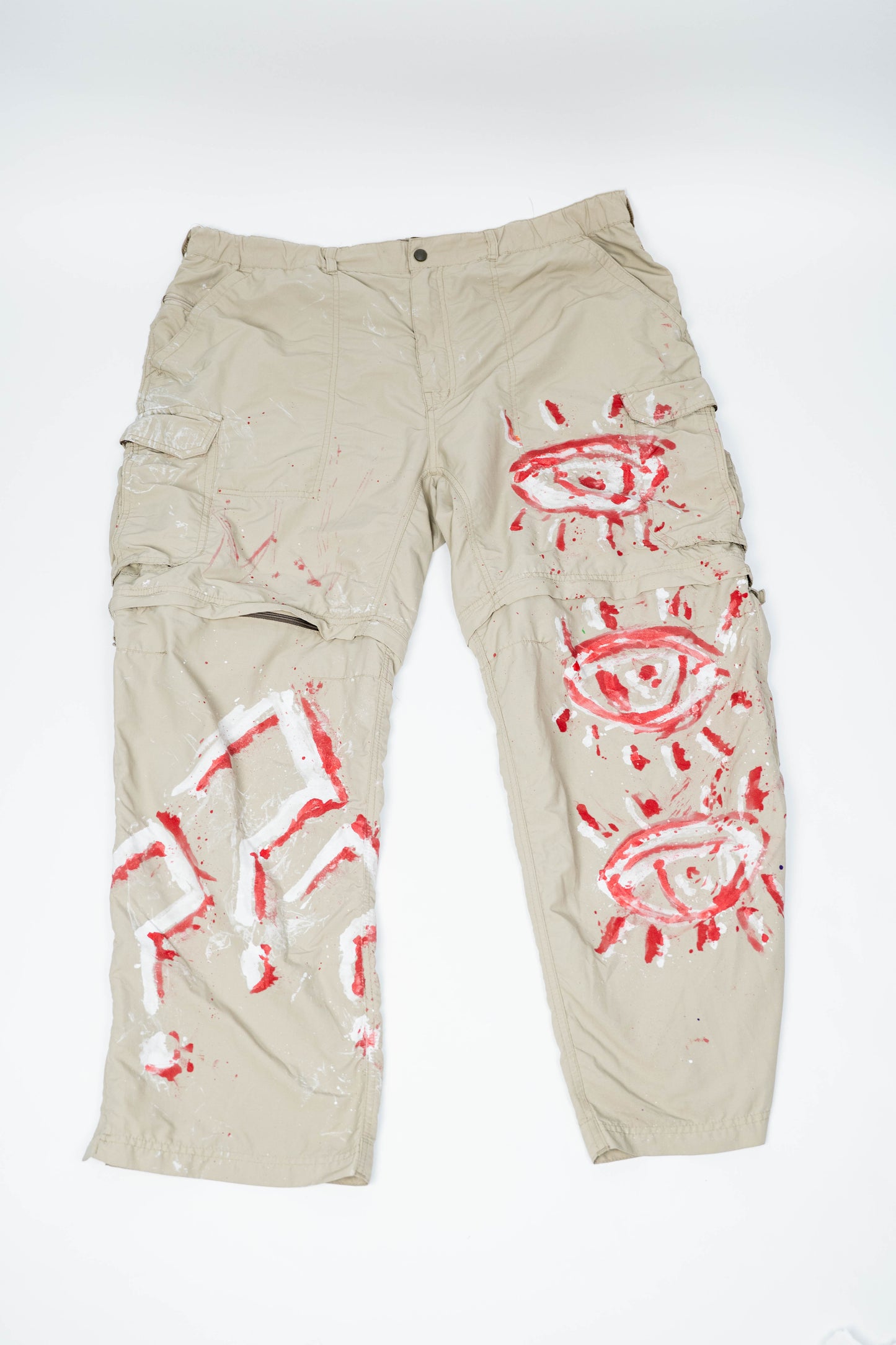 Beige cargo pants with red and white spray painted designs on a white background