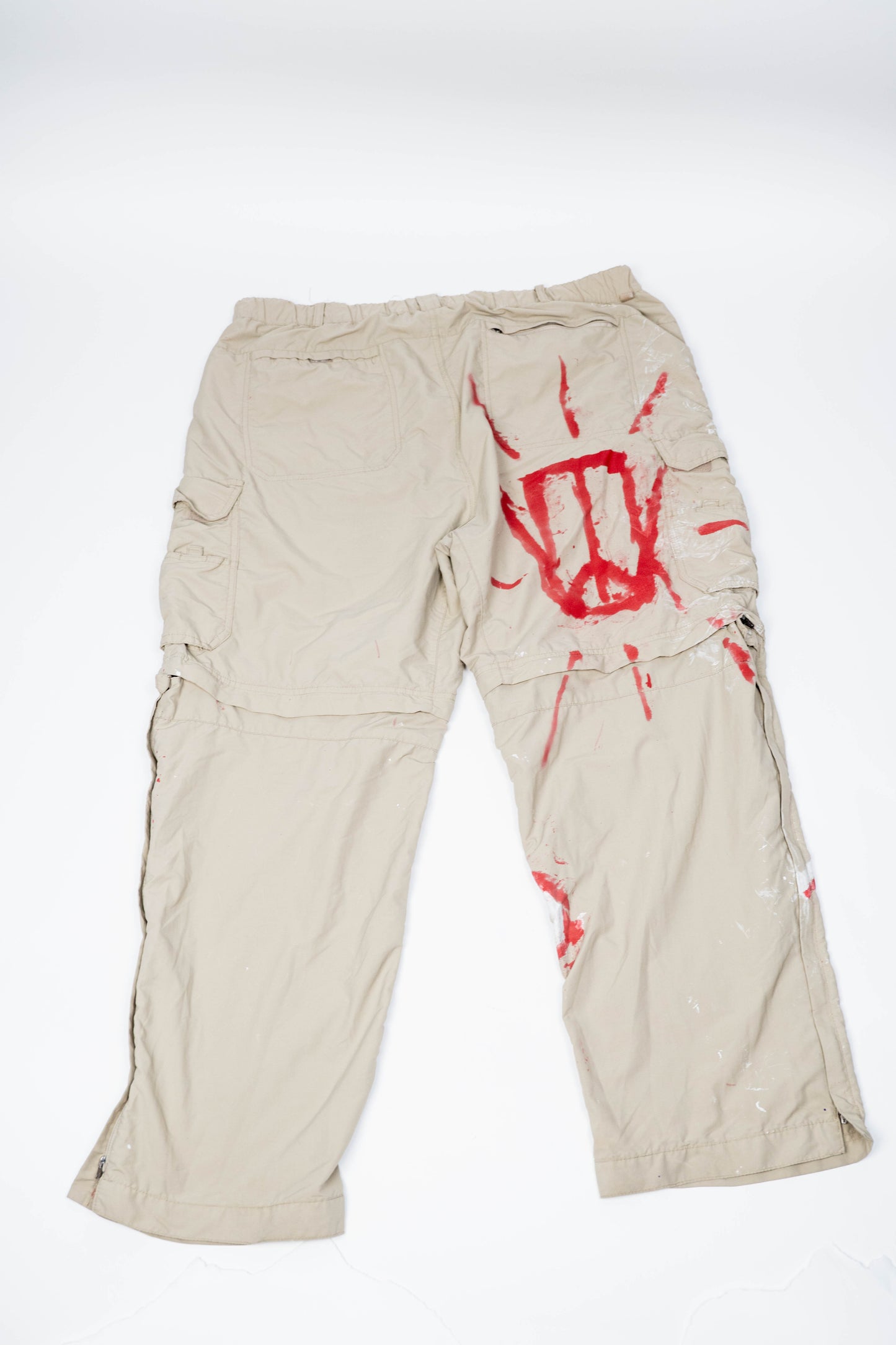 Beige cargo pants with red spray painted logo on a white background