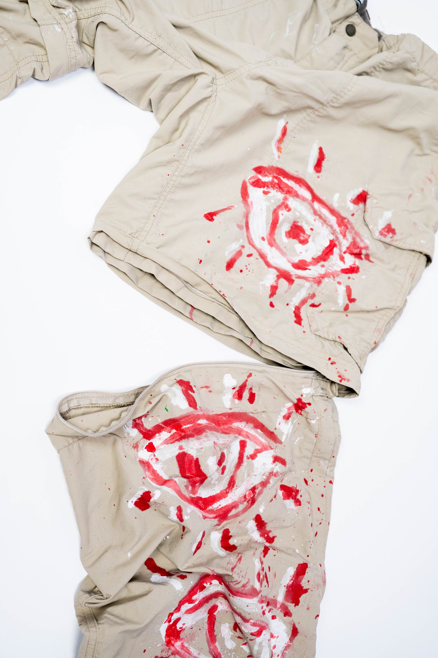 Beige pants with red and white spray painted eye designs showing ability to convert into shorts on a white background