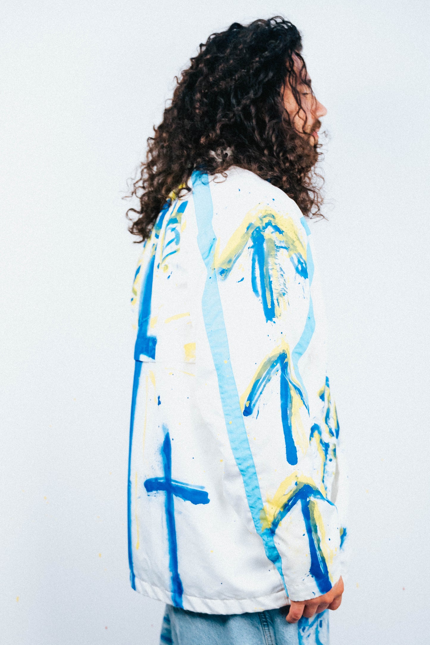 Person wearing a white jacket with blue and yellow abstract spray painted patterns on a plain background