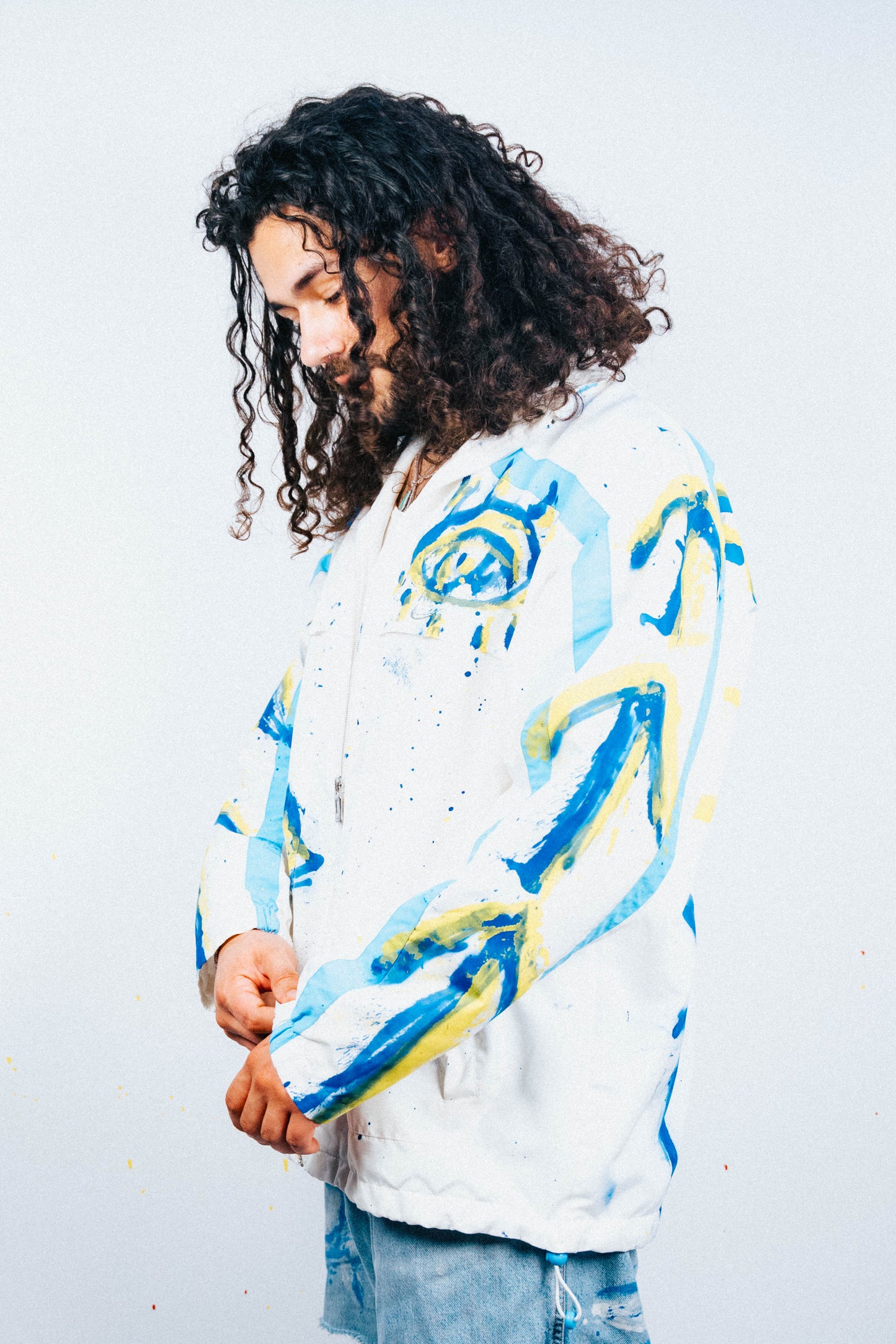 Person wearing a white jacket with blue and yellow abstract spray painted designs on a plain background