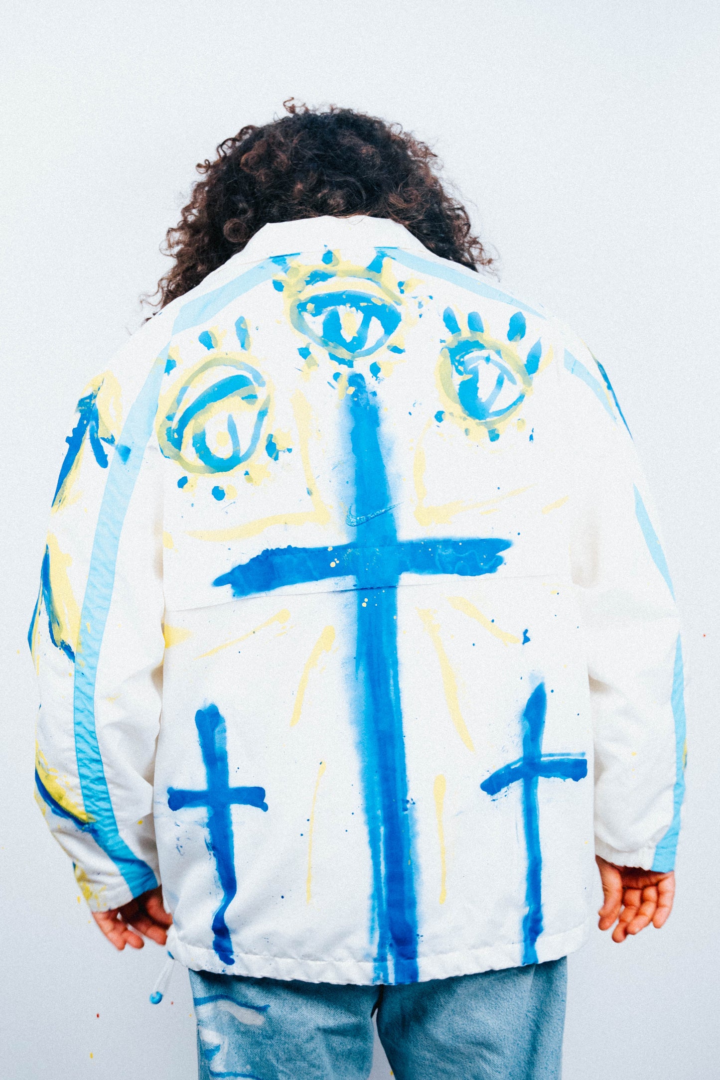 Person wearing a white jacket with blue and yellow painted designs on a plain background