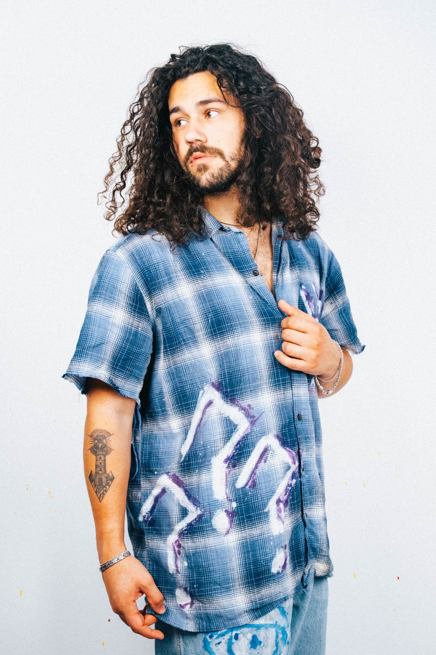 Man wearing a blue plaid shirt with white and purple spray painted graphic design on a plain background