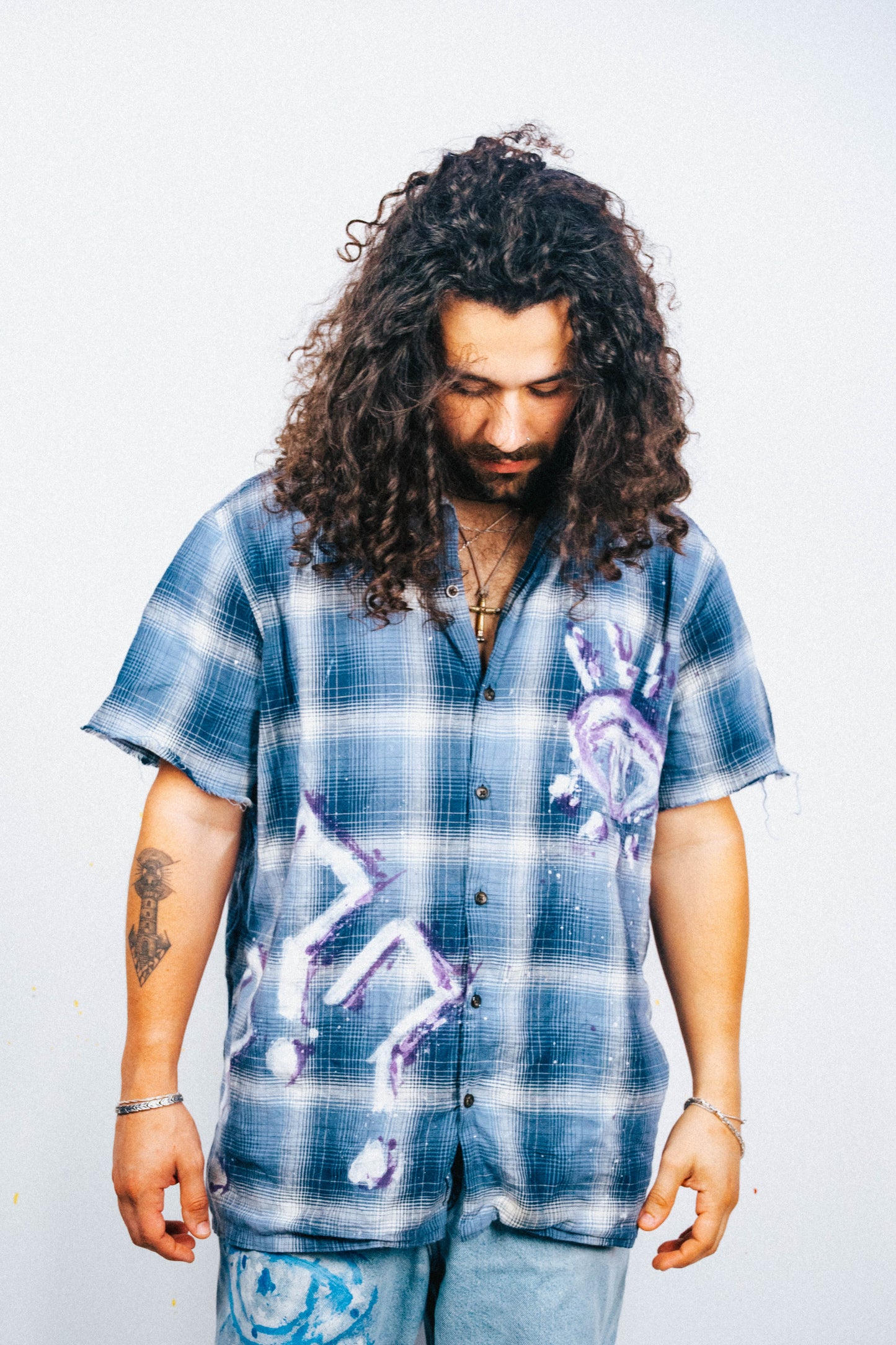 Man wearing a blue plaid shirt with white and purple spray painted graphic designs on a plain background