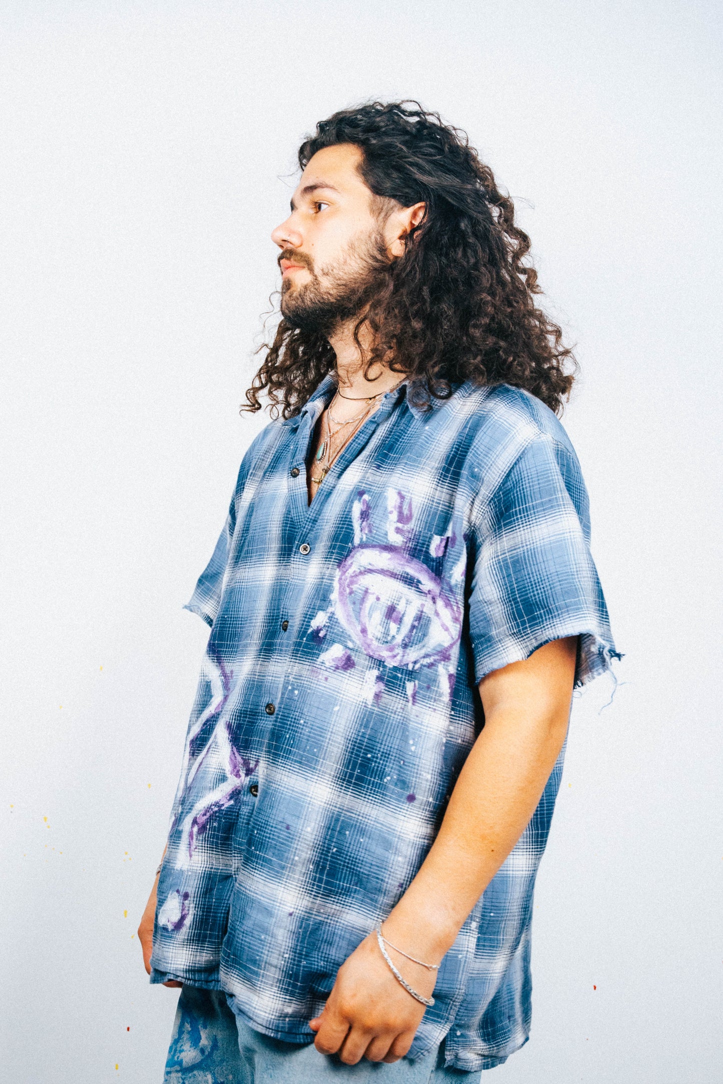Man wearing a blue plaid shirt with a white and purple spray painted graphic design on a white background