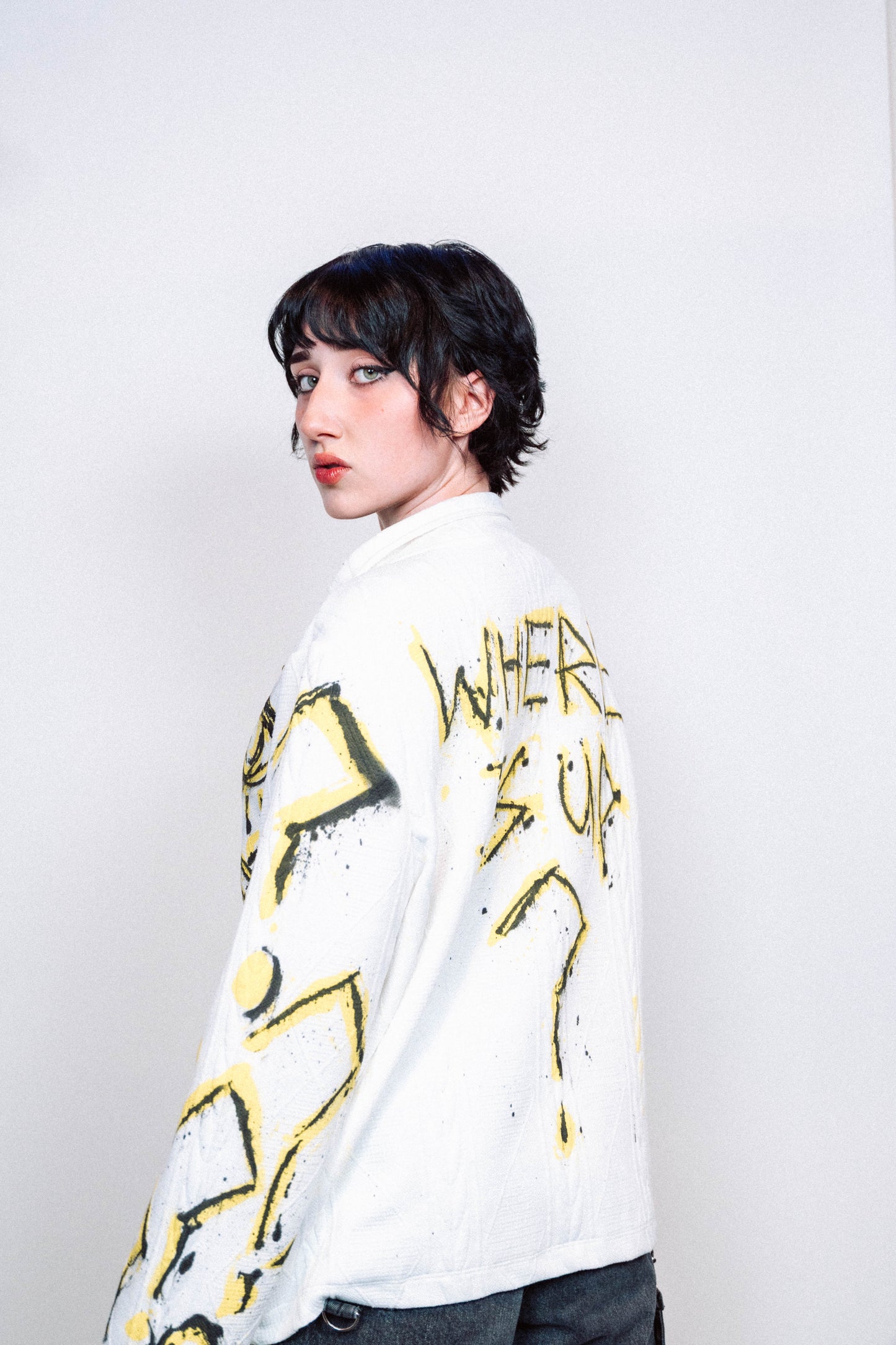 Person wearing a 1 of 1 Spray Painted white jacket with yellow designs on a plain background