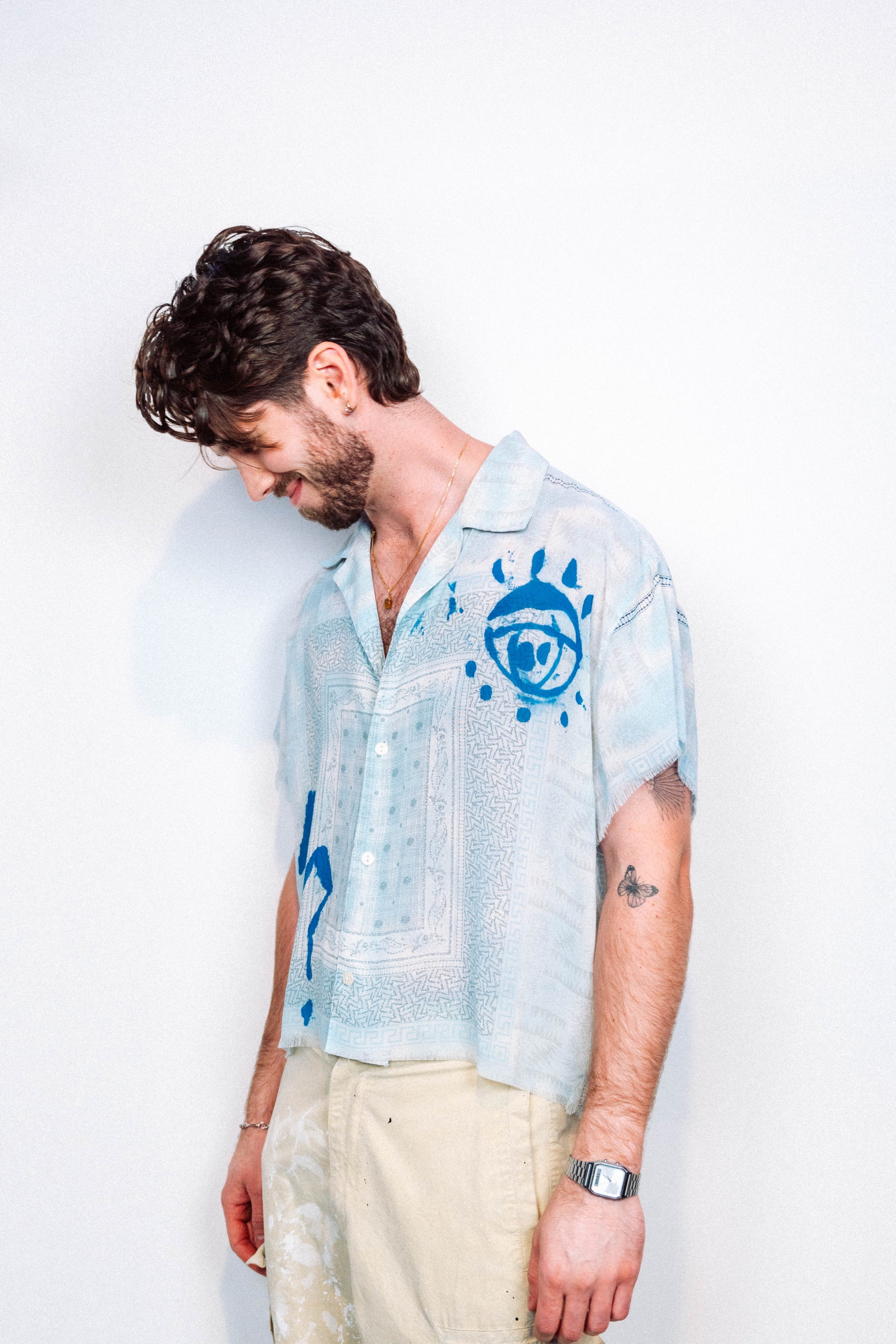 Person wearing a light blue 1 of 1 spray painted button up from "where is up" with blue patterns on a white background