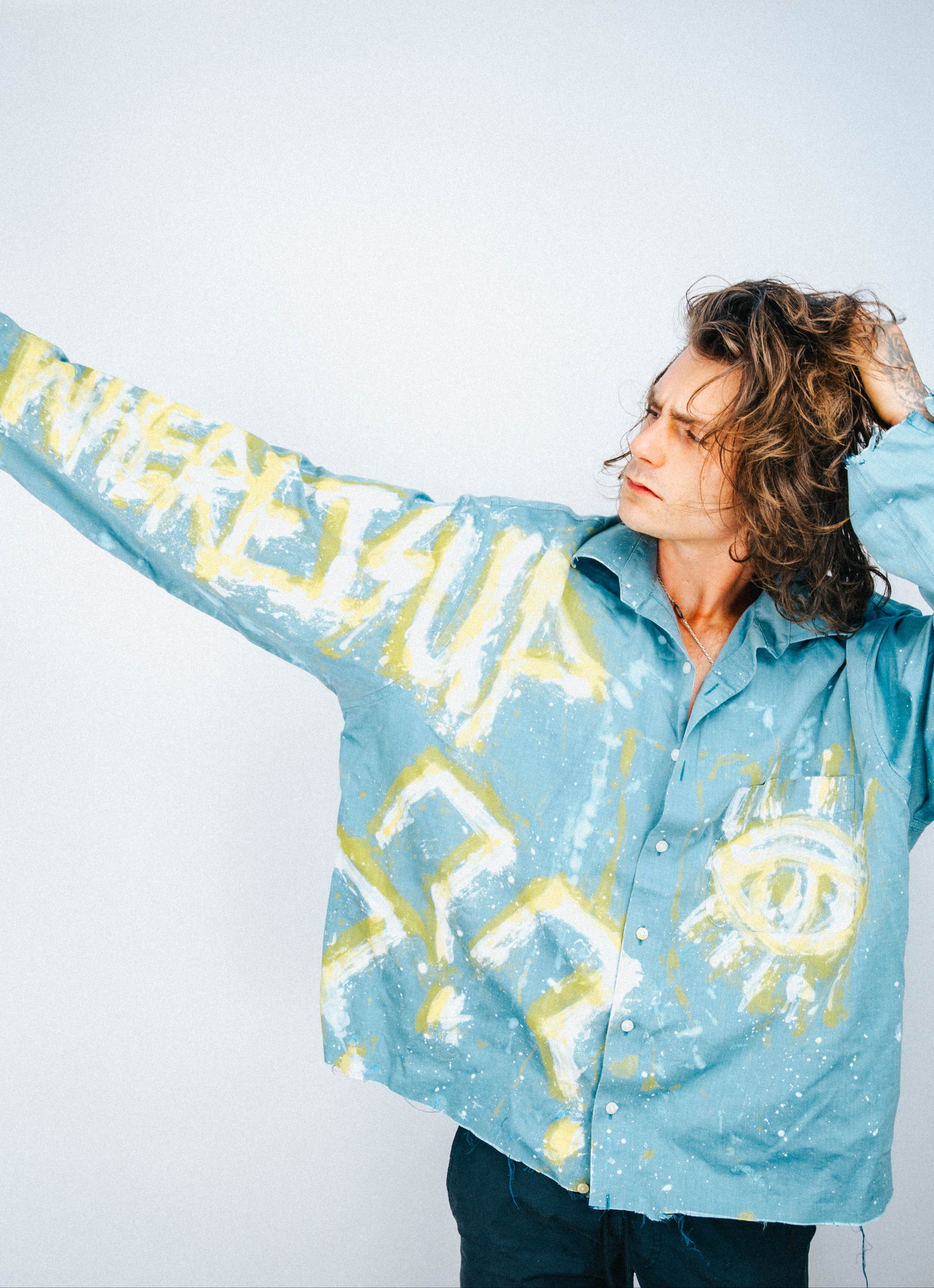 Man wearing a light blue shirt with abstract white and yellow spray painted designs on a plain background