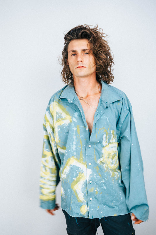 Man wearing a light blue shirt with abstract spray painted designs on a plain background
