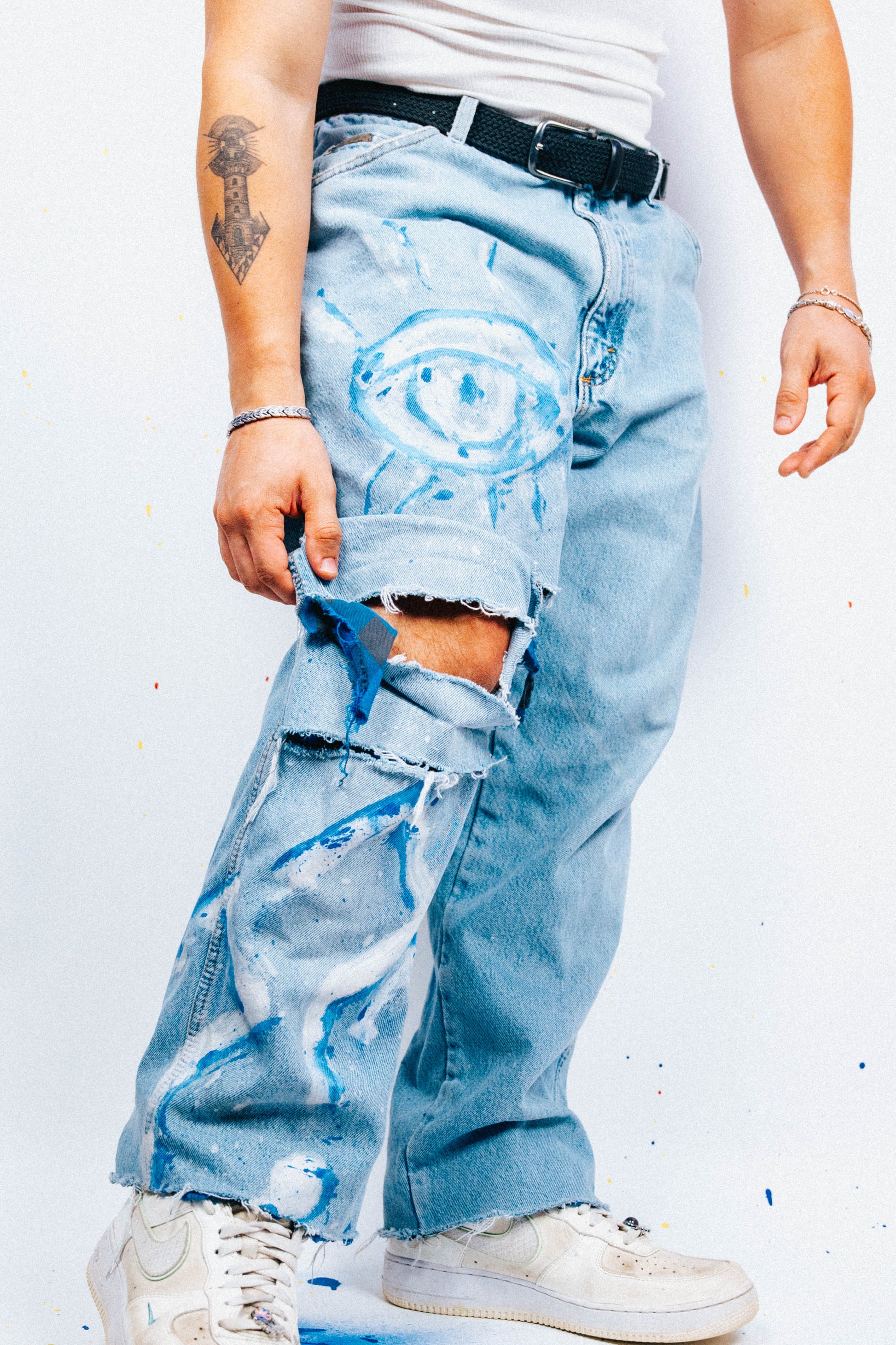 Person wearing light blue jeans with 1 of 1 hand painted graphics on a white background