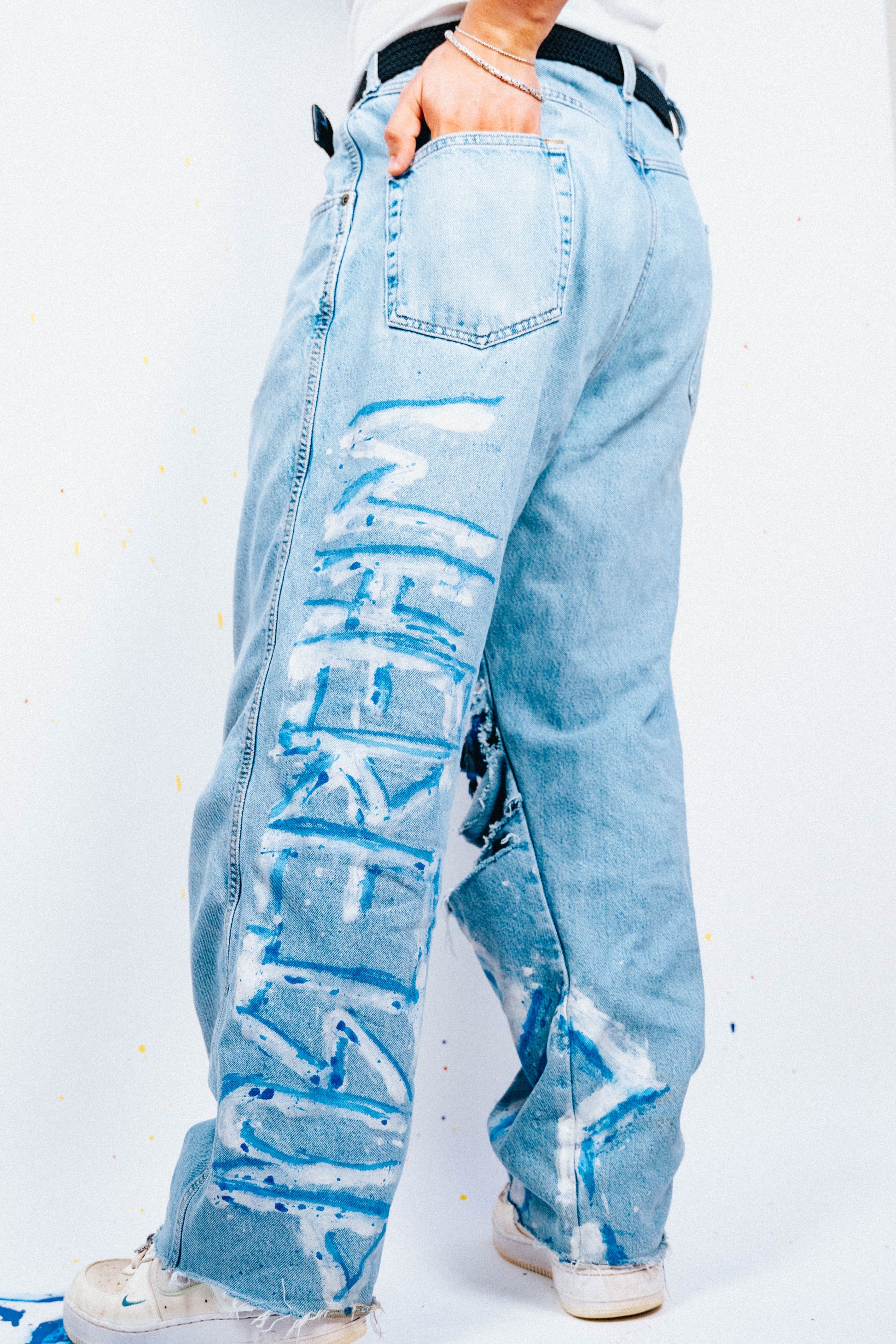 Light blue 1 of 1 spray painted and distressed jeans worn by a person on a white background
