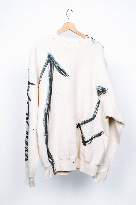 Cream colored 1 of 1 sweater with black abstract spray painted designs on a hanger against a white background