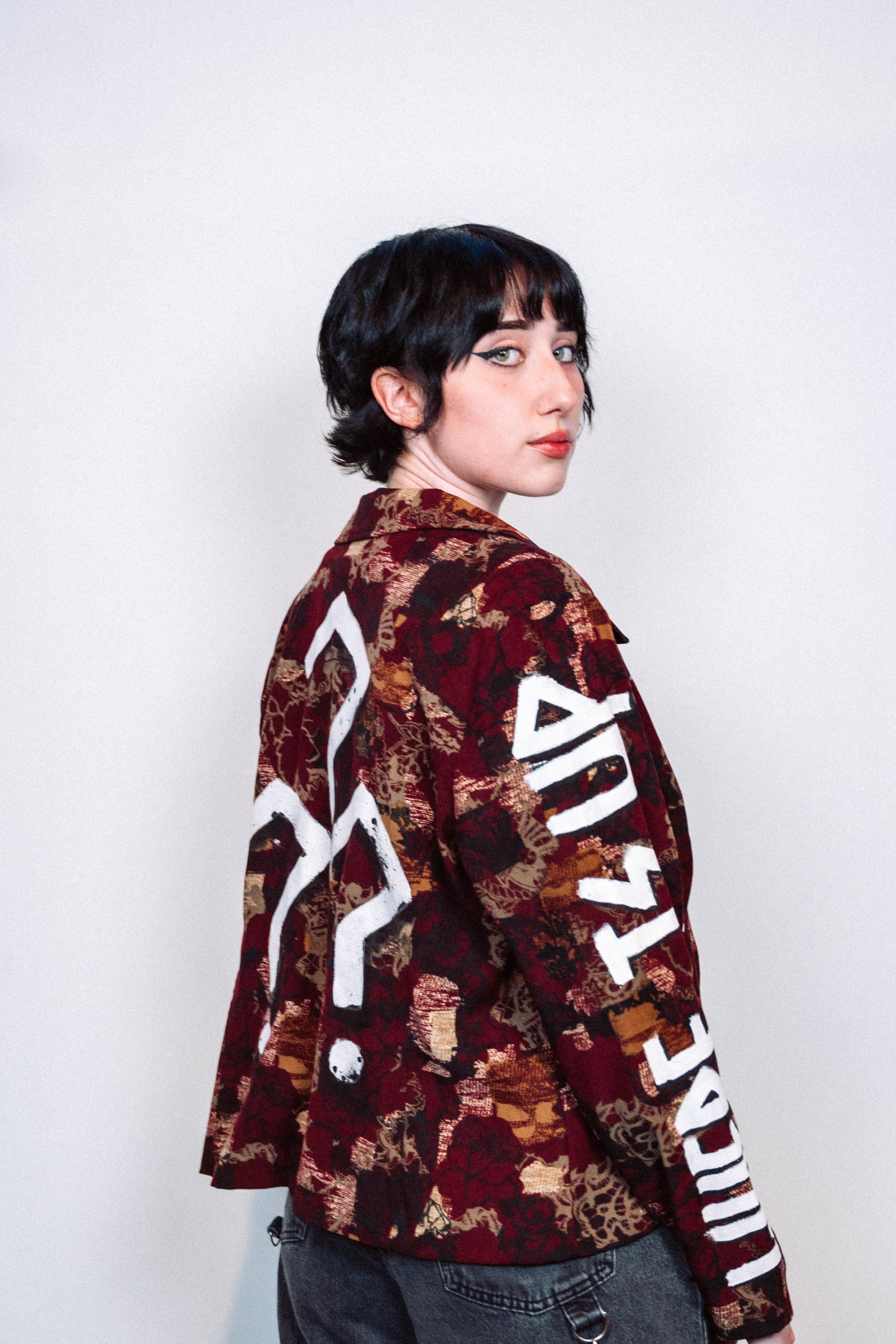 girl wearing a 1 of 1 hand painted pattern jacket with white paint in front of a white background