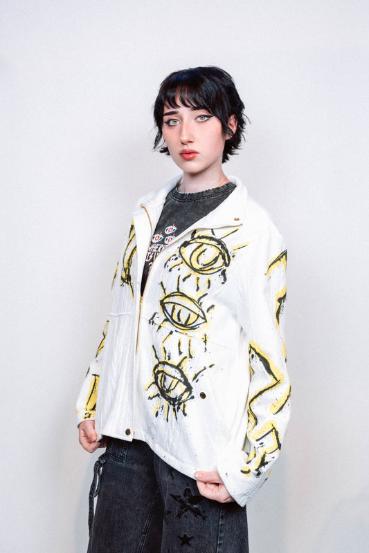 Person wearing a 1 of 1 Spray Painted white jacket with yellow designs on a plain background