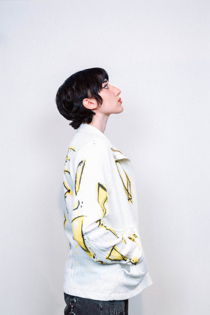 Person wearing a 1 of 1 Spray Painted white jacket with yellow designs on a plain background