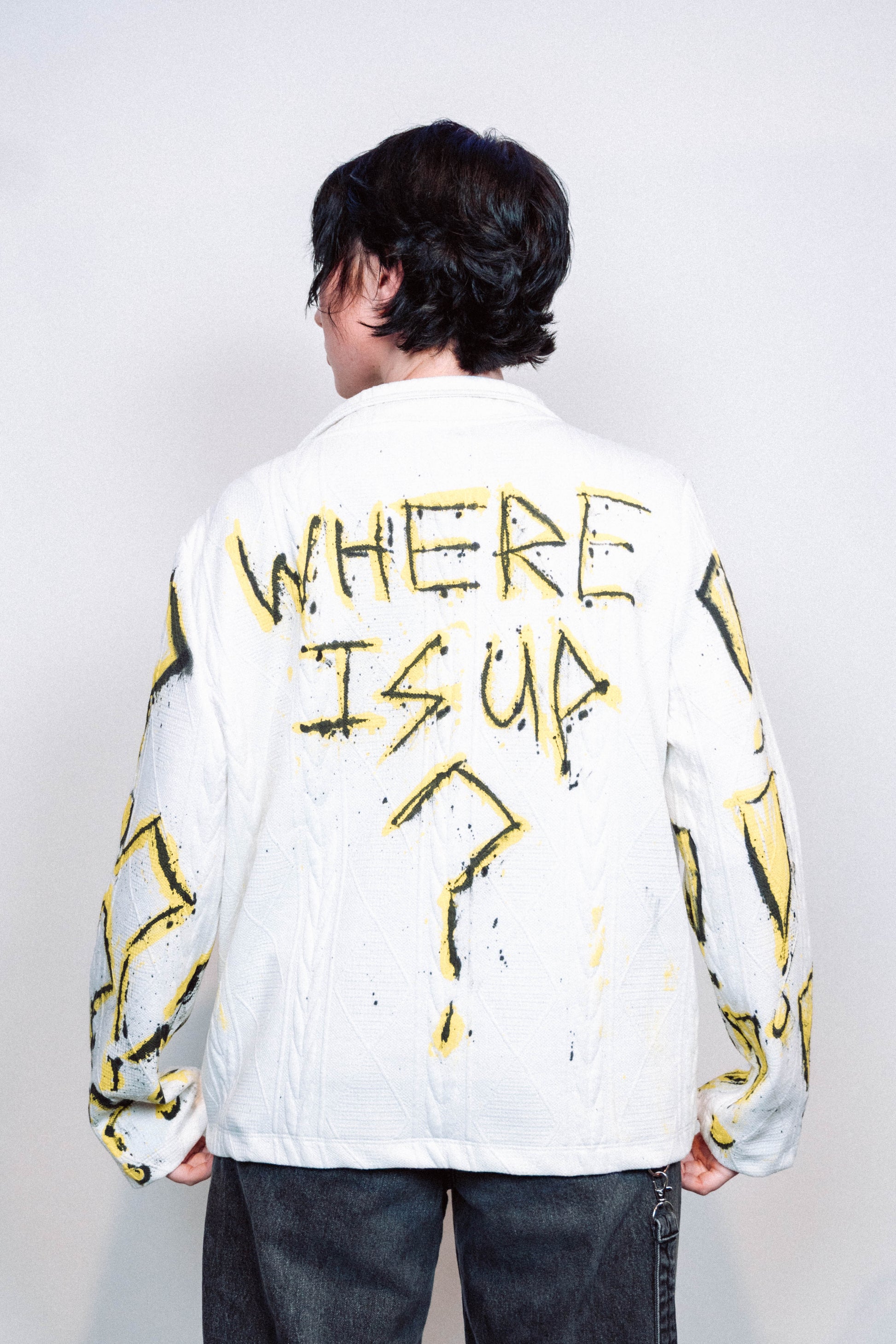 Person wearing a 1 of 1 Spray Painted white jacket with yellow designs on a plain background