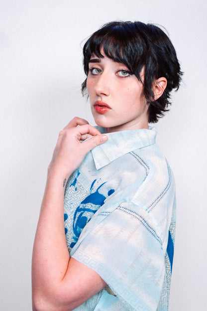 Person wearing a light blue 1 of 1 spray painted button up from "where is up" with blue patterns on a white background