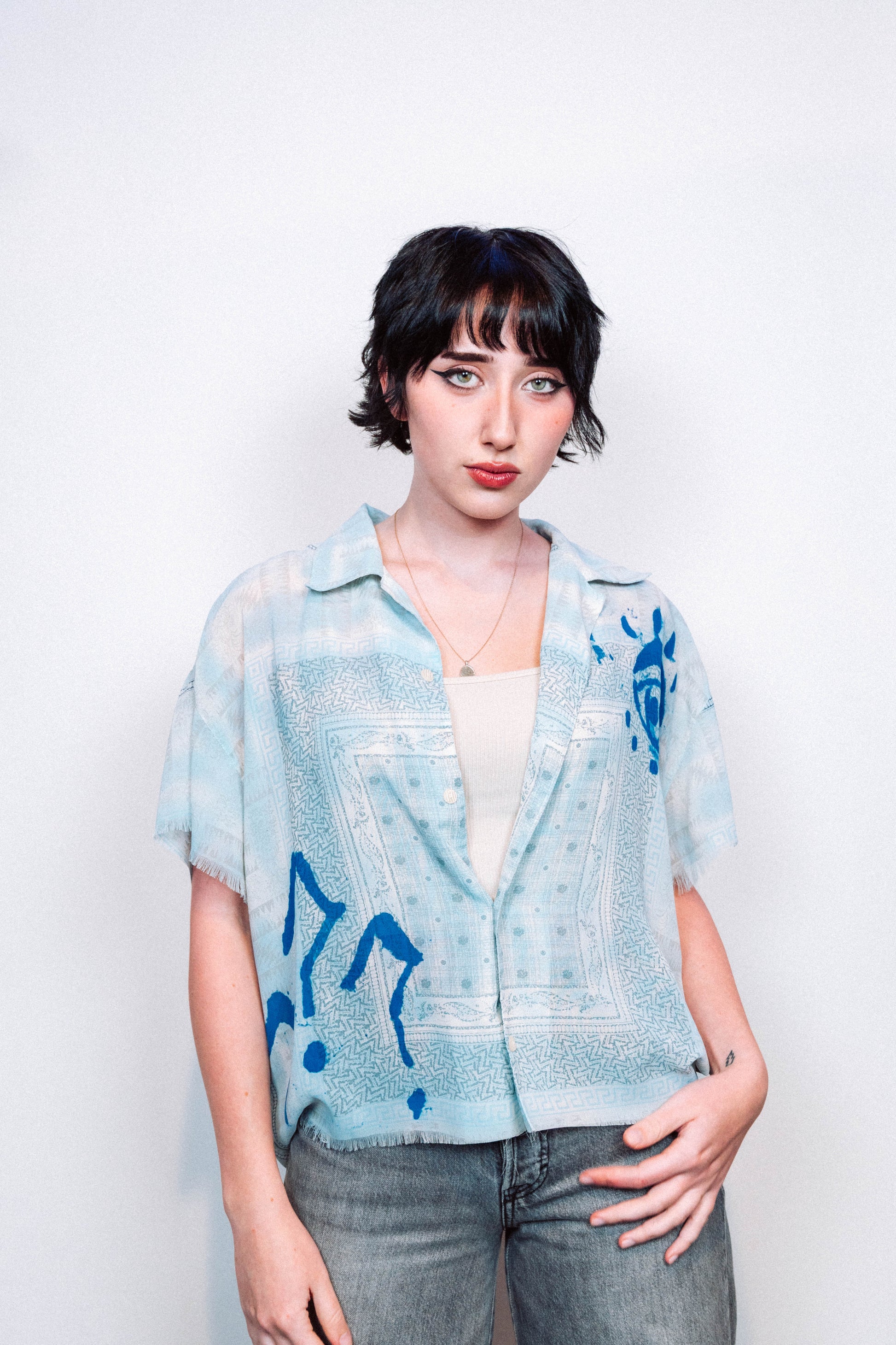 Person wearing a light blue 1 of 1 spray painted button up from "where is up" with blue patterns on a white background
