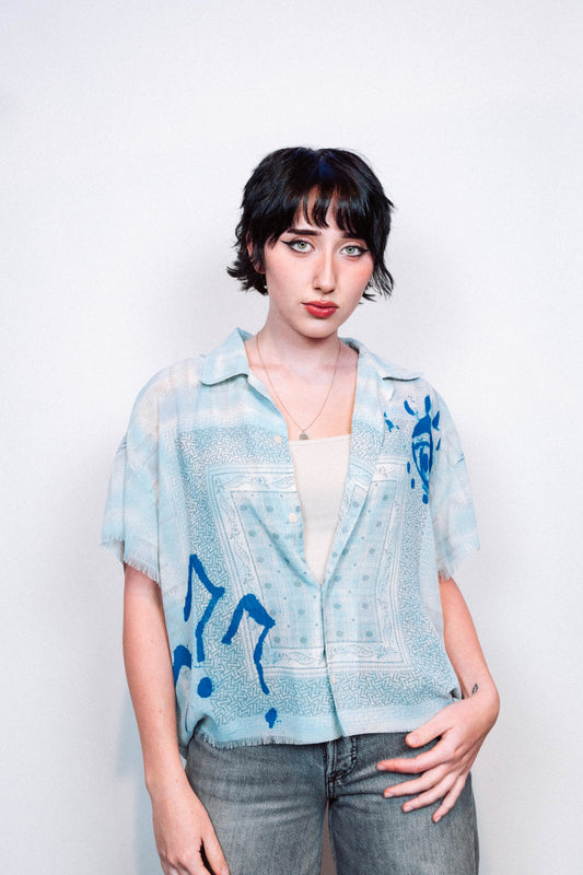Person wearing a light blue 1 of 1 spray painted button up from "where is up" with blue patterns on a white background